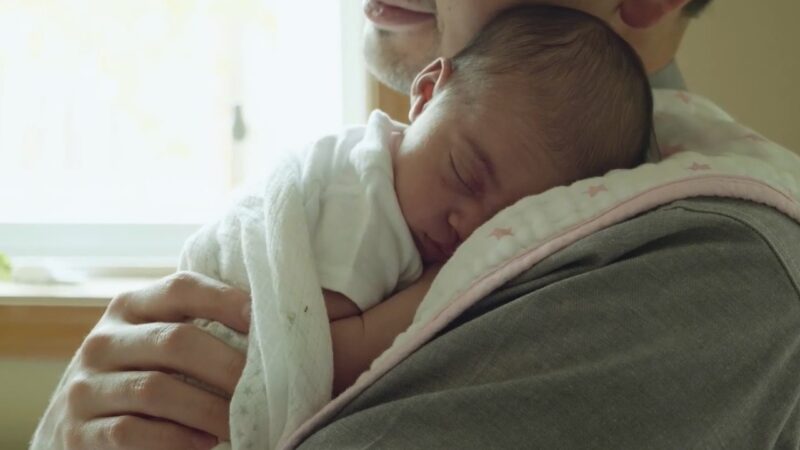 A Newborn Baby Peacefully Sleeps on An Adult’s Shoulder