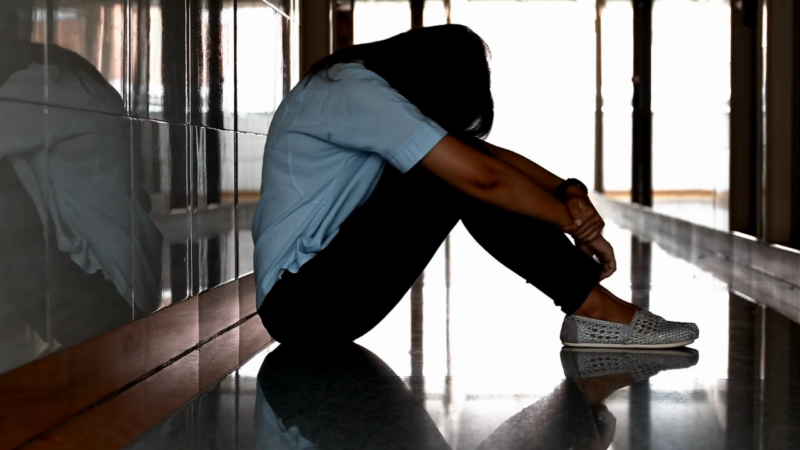 A Teen Girl Sits Alone on The Floor with Her Head Down, Looking Anxious