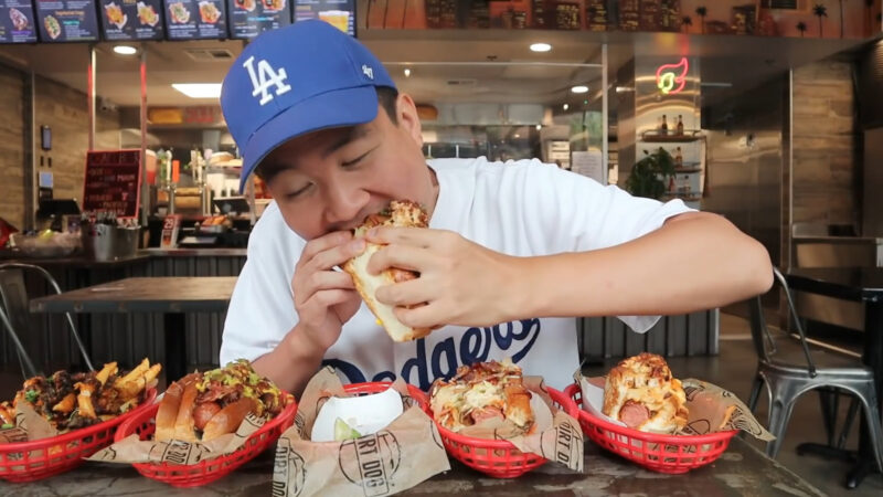 A Person Wearing a Blue Dodgers Cap Enjoys a Loaded Hot Dog Inside the Dirt Dog Restaurant