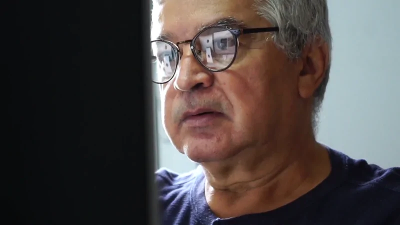 An Older Man Wearing Glasses Works at A Computer