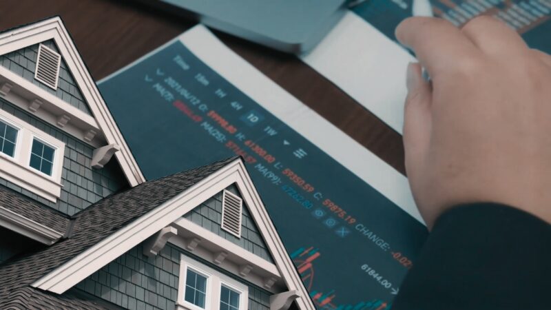 A Close-Up of A Traditional House's Roofline Overlaid on A Background of A Person Reviewing Financial Graphs and Data on Paper, Symbolizing the Analysis and Planning Involved in Advancing Philadelphia's Housing Market and Future Development