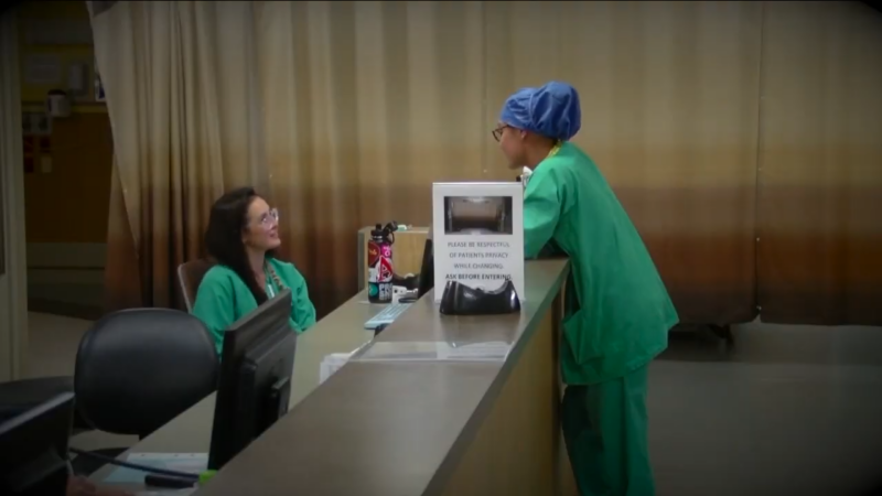 Two Healthcare Professionals in Green Scrubs Conversing at A Hospital Reception Desk, Reflecting the Collaborative and Patient-Focused Environment Within Colorado's Healthcare System