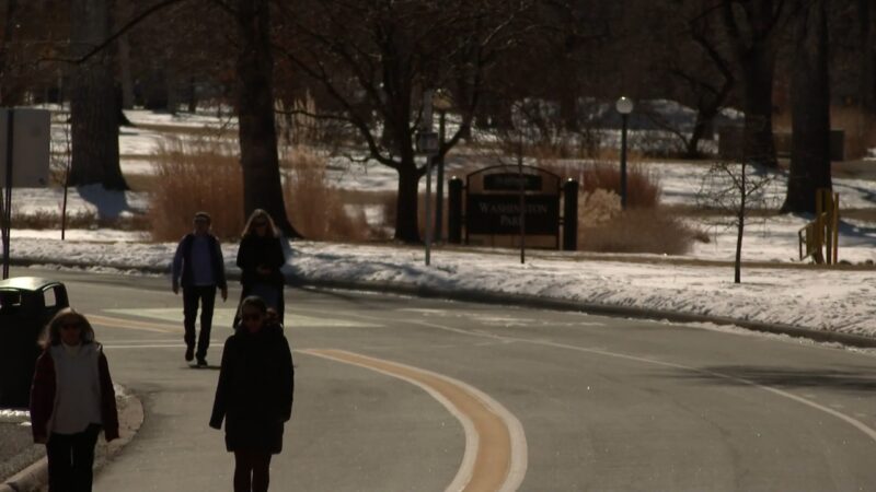 People Walking Along a Curved Road in Washington Park During Winter, with Snow on The Ground and Bare Trees in The Background