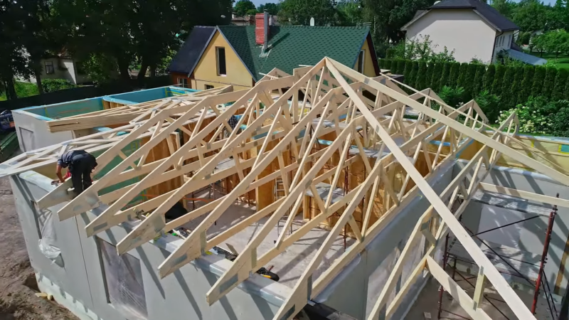  A Partially Constructed House with Wooden Roof Trusses Being Assembled, Indicating Active Development and Construction Trends in The Housing Market, with Surrounding Homes and Greenery Visible in The Background