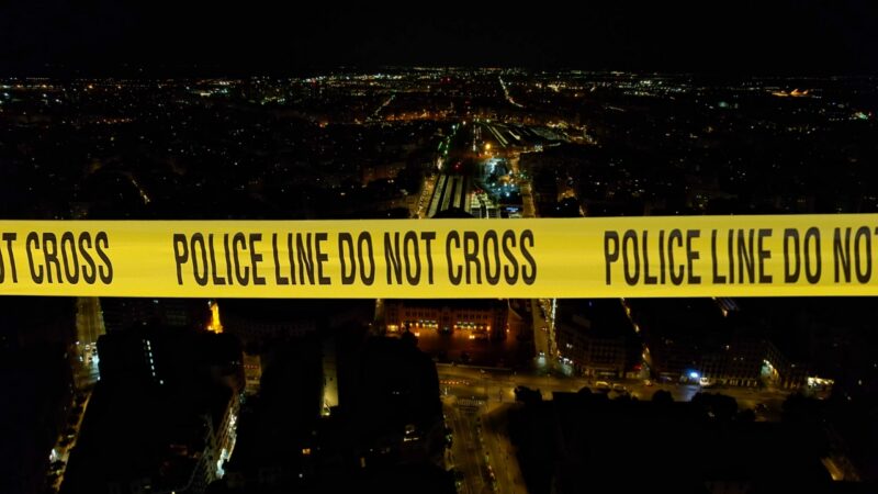 Aerial Night View of A Cityscape Intersected by A Large Yellow Police Tape Reading "Police Line Do Not Cross," Highlighting a Focus on Crime Trends in Valencia