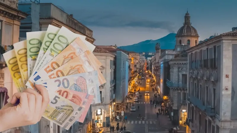 A View of A Sicilian Street at Dusk with A Hand Holding Various Euro Banknotes