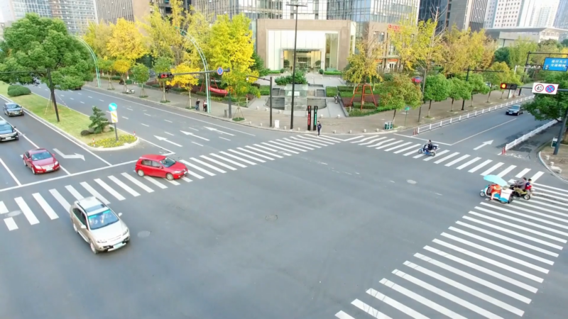 Aerial View of A Bustling Urban Intersection with Marked Crosswalks and Varied Traffic Amidst Greenery and Modern Buildings