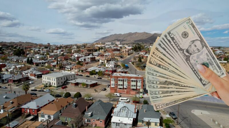 Aerial View of A Residential Area in El Paso with A Hand Holding a Fan of U.S. Dollar Bills in The Foreground, Representing the Concept of Median Household Income in The City