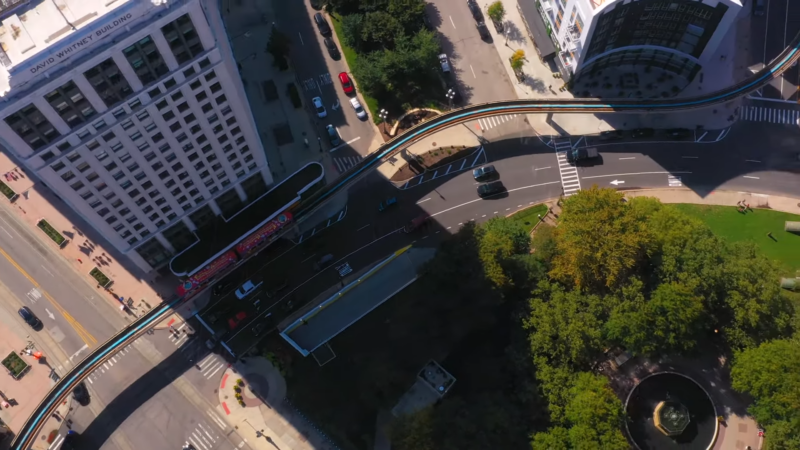 An Aerial View of Downtown Detroit, Michigan in 2024, Showing the David Whitney Building, a Monorail System, Green Spaces, and Surrounding Streets with Vehicles and Pedestrians