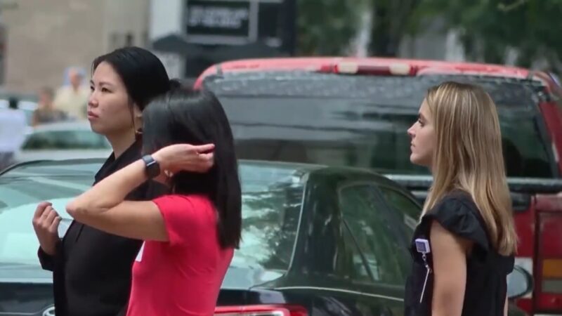 Three Women Standing on A City Street, Two Talking and Gesturing While the Third Looks Away