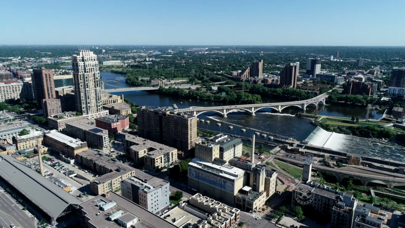 The Image Shows an Aerial View of Downtown Minneapolis, Featuring High-Rise Buildings, Bridges, and The Mississippi River, Representing the City's Development and Population Growth in 2024