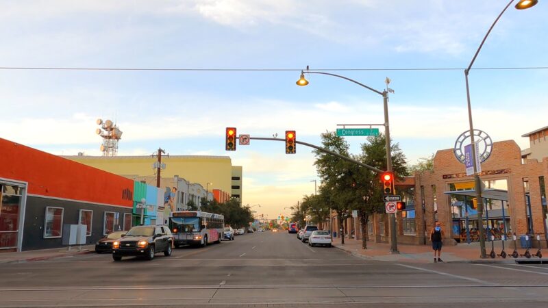 View of A Bustling Street in Tucson with Cars, a Bus, and Pedestrians Under Traffic Lights and Street Signs at Sunset