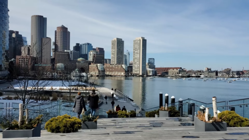 View of Boston's Skyline Featuring Modern High-Rise Buildings and A Bustling Waterfront Park, with People Walking Along the Promenade