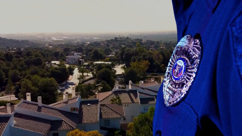 Aerial View of A Suburban Area in Valencia, Spain, Overlaid with A Close-Up of A Sparkling Police Badge, Symbolizing a Focus on Property Crimes