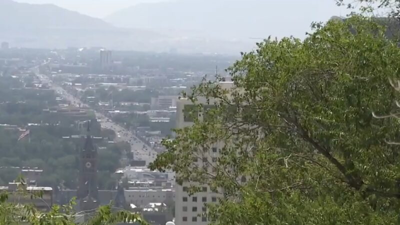 A Hazy View of A Growing Urban Area in Utah, Framed by Trees, Showing Downtown Buildings and Distant Mountains, Symbolizing Population Expansion