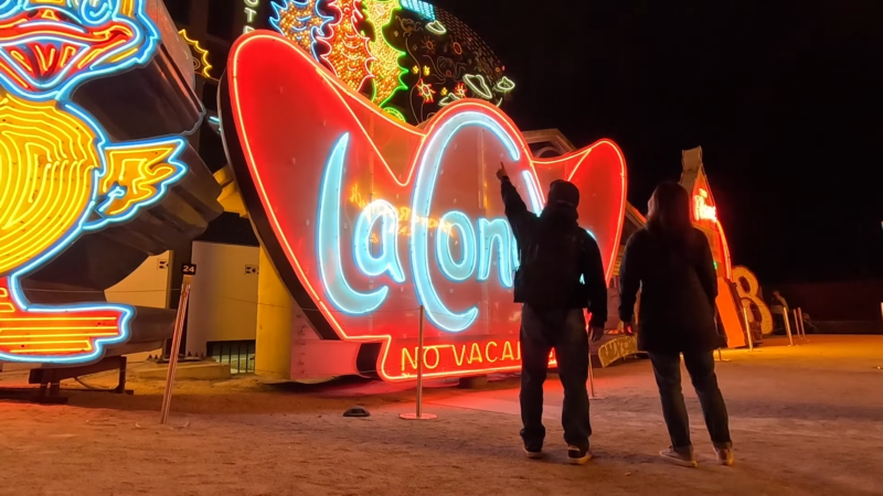 Two People Admire Vibrant, Restored Neon Signs at The Neon Museum in Las Vegas at Night