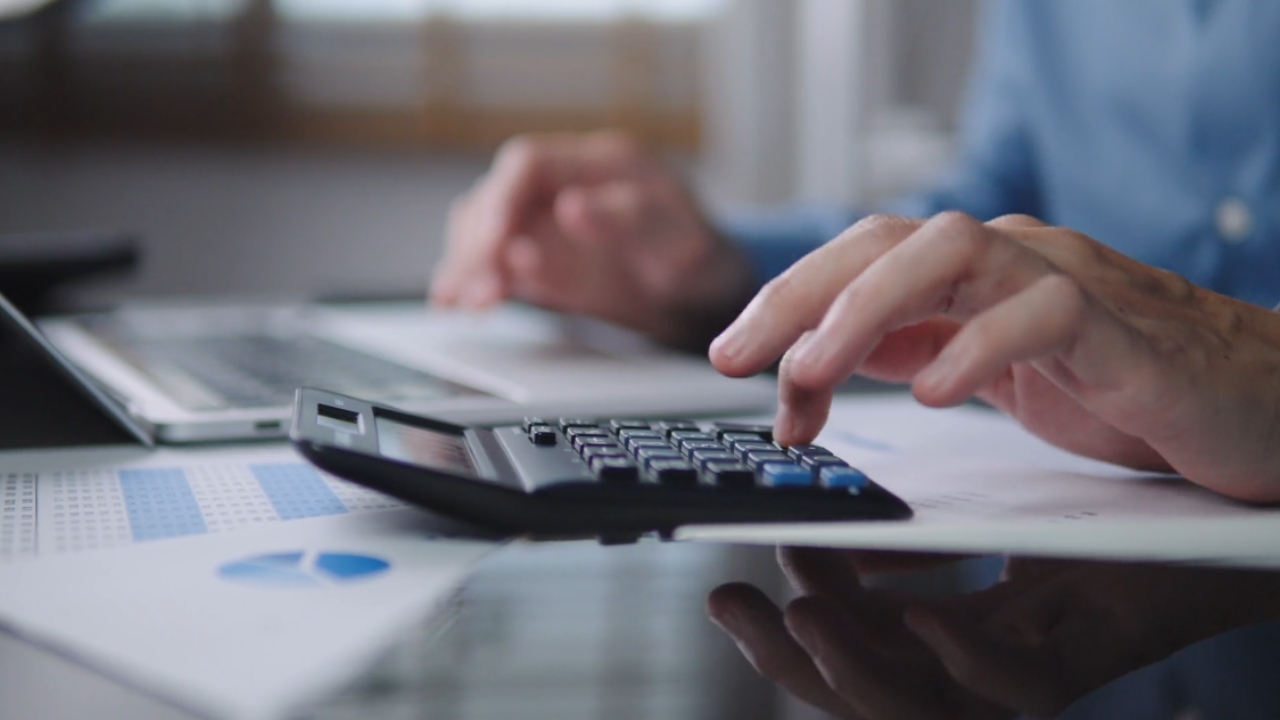 Person uses a calculator beside financial papers on a desk