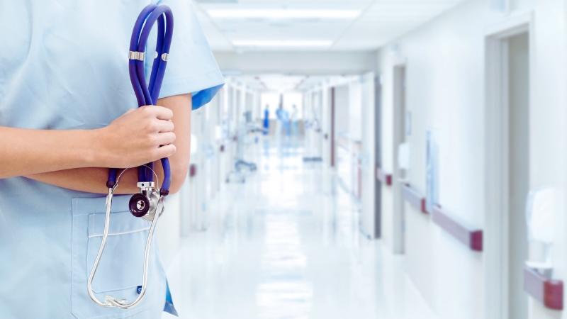 A Healthcare Worker Holds a Stethoscope in A Hospital Hallway