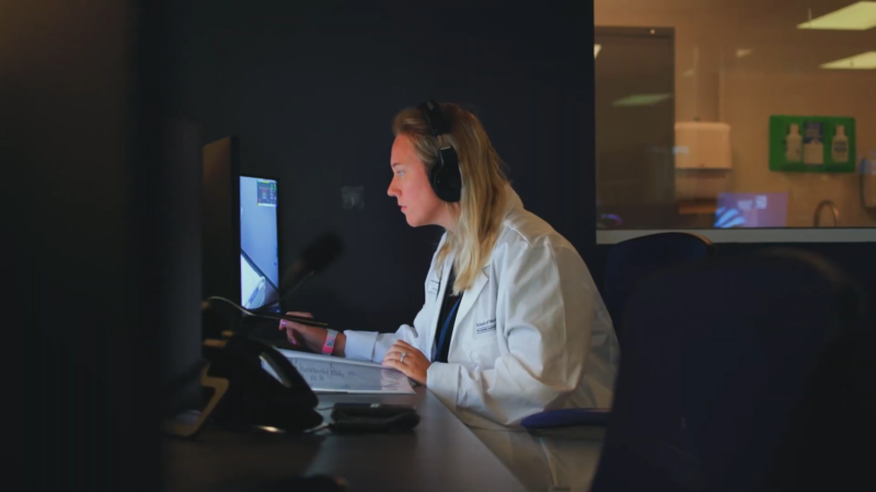 Female Healthcare Professional in A Lab Coat Wearing Headphones, Working on A Computer in A Clinical or Educational Setting