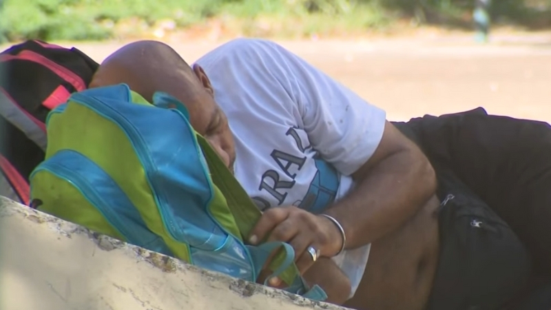 A Man Is Lying Down Outdoors with A Backpack, Reflecting the Situation of Homelessness in Miami Beach