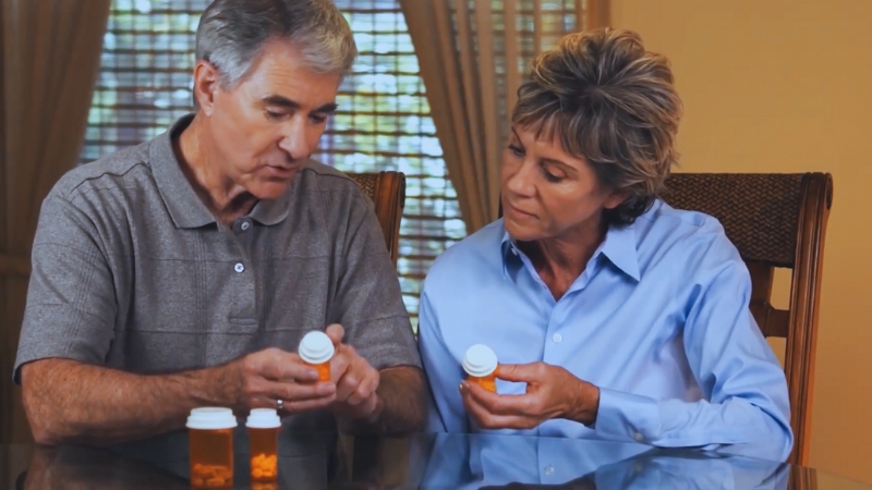 An Older Couple Is Seated at A Table, Closely Examining Prescription Medication Bottles