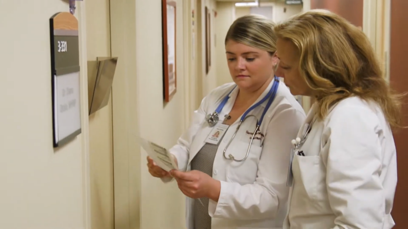 Two Nurses Review Medical Documents Together in A Hospital Hallway