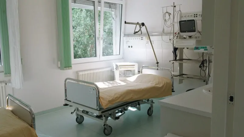 The image shows an empty hospital room with a bed and medical equipment