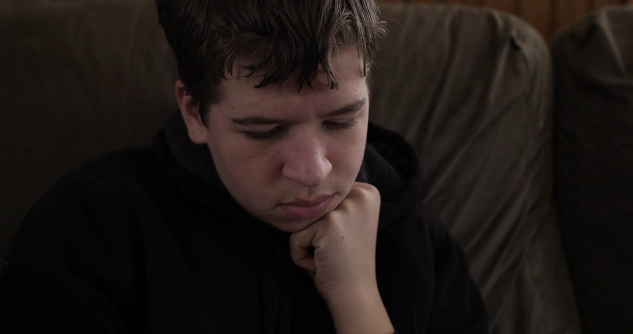 A teenage boy sitting on a couch, looking down in contemplation or sadness