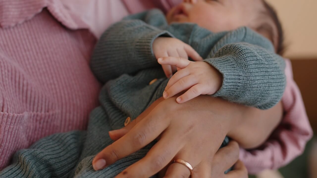 A baby wearing a knitted sweater asleep in the arms of a caregiver