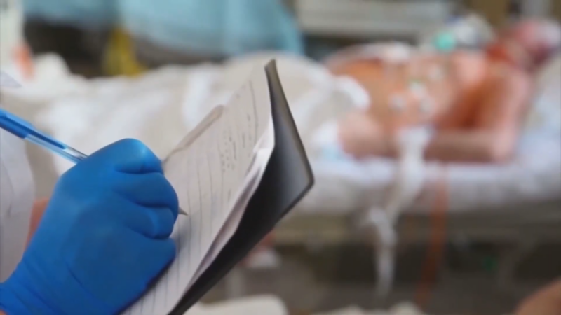 A Healthcare Worker Taking Notes Beside a Patient in Critical Care