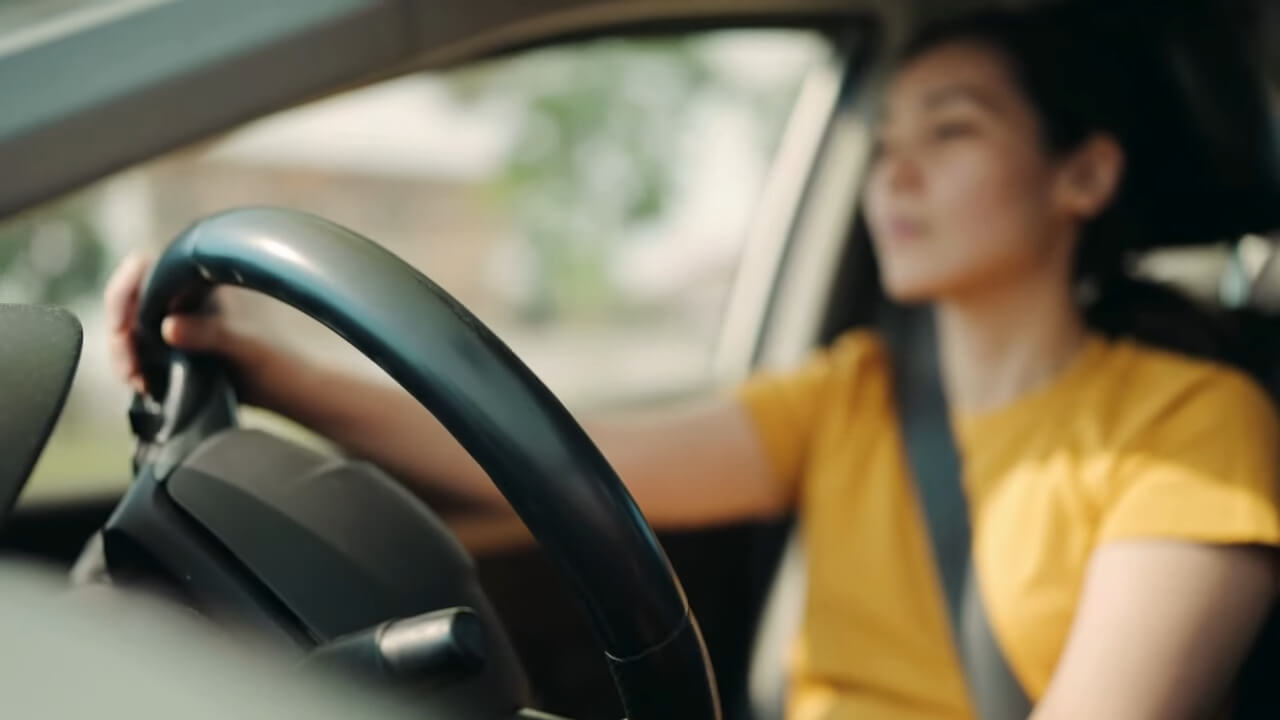 A young woman wearing a yellow shirt focuses on driving