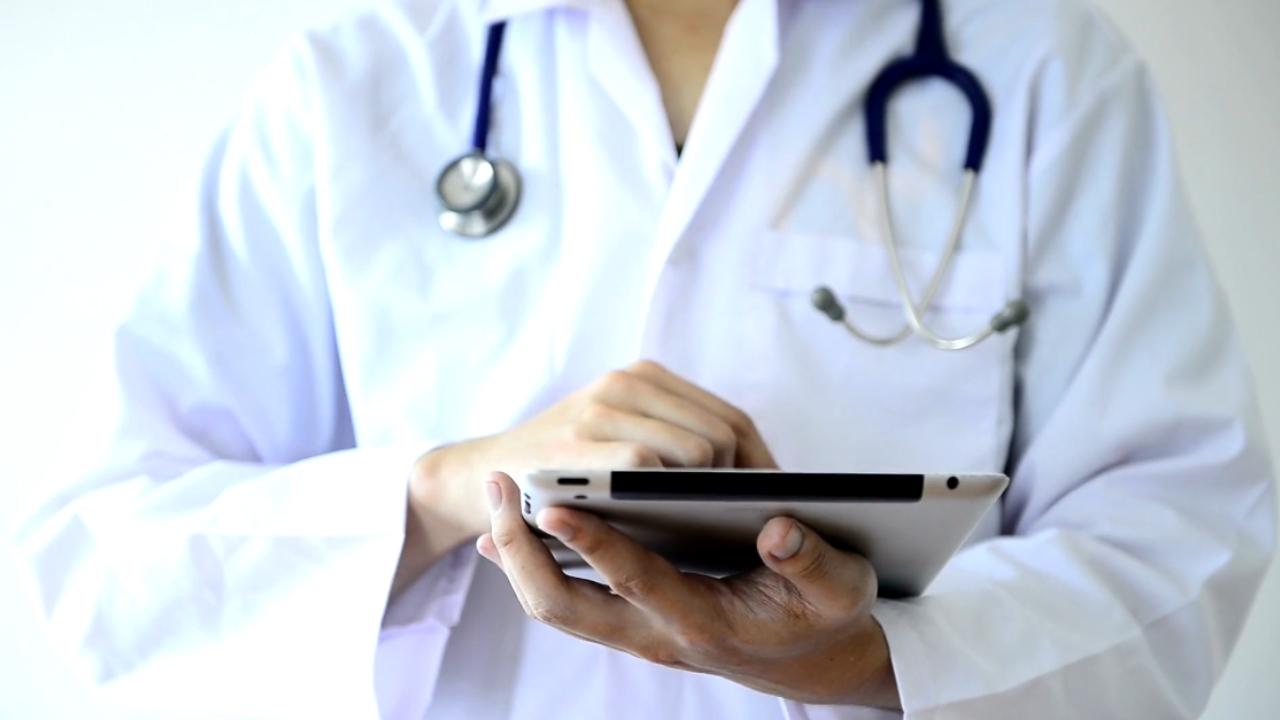 A doctor in a white coat uses a tablet