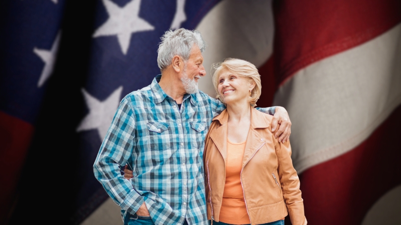 Smiling Elderly Couple Standing in Front of The U.S. Flag, Representing Us Life Expectancy Trends