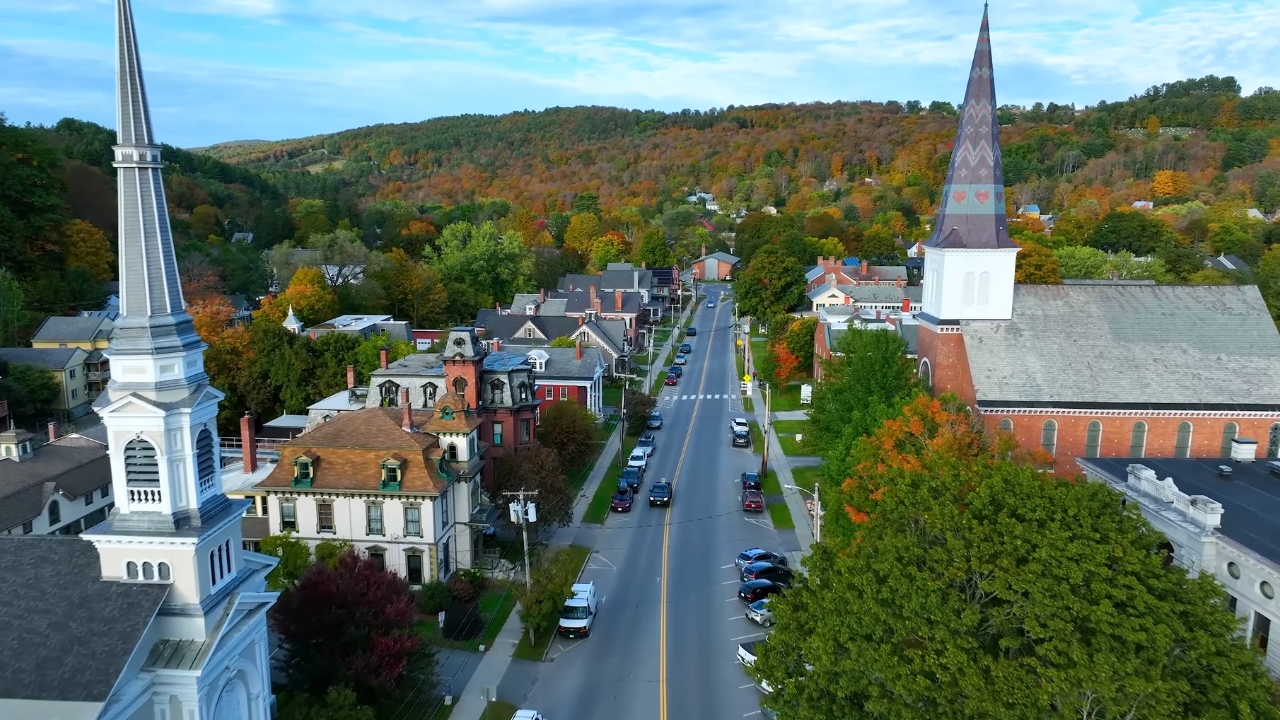 A Vermont town street runs past church steeples and autumn hills