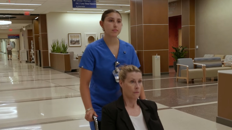 A Medical Assistant Pushing a Patient in A Wheelchair Through a Healthcare Facility