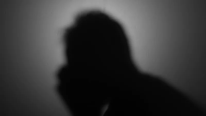 The image shows the shadow of a person with their hand on their face, conveying a moment of distress