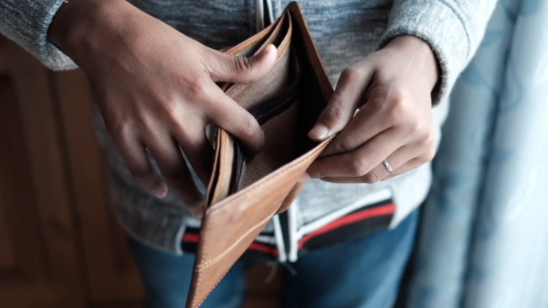 Person holding an empty wallet, showing no money inside