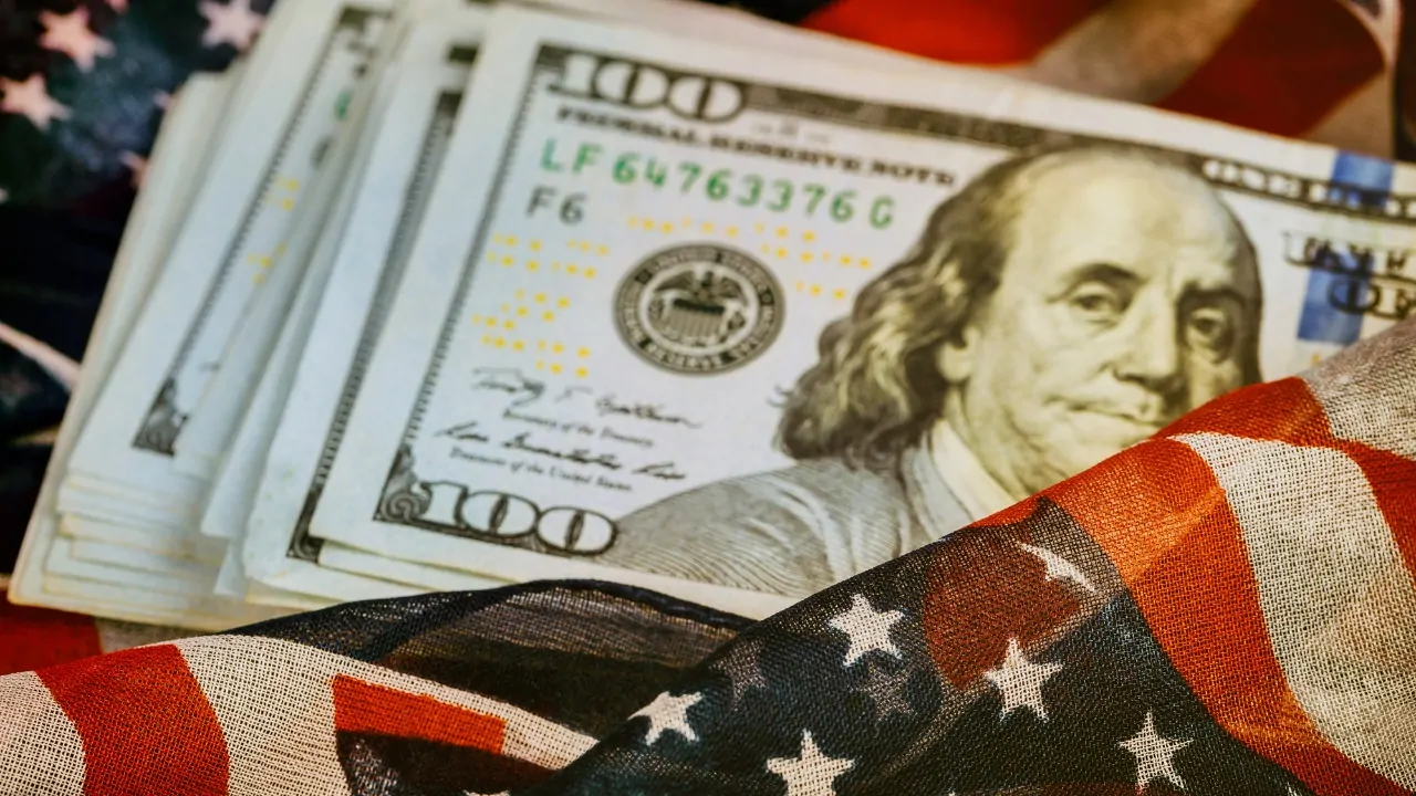 Stacks of U.S. dollar bills sit beside an American flag
