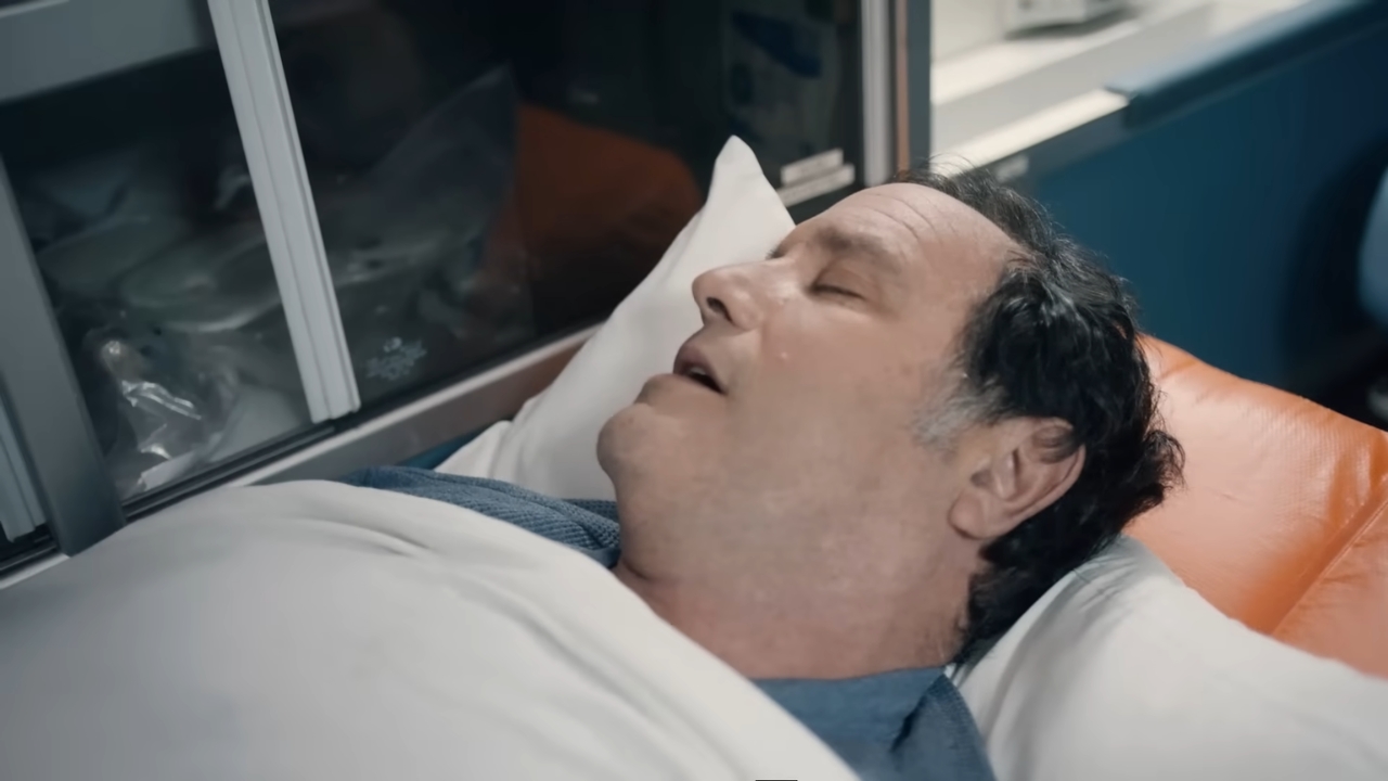 A man lies on a hospital stretcher with his eyes closed