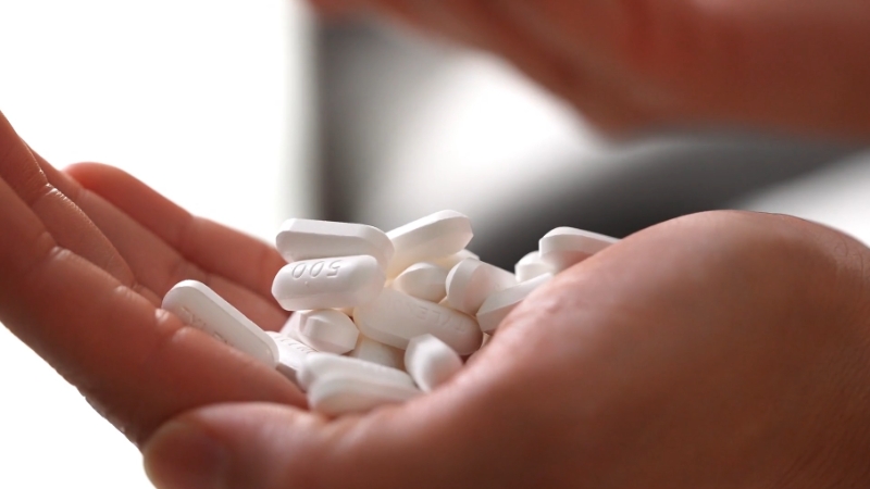 A hand holding multiple white opioid tablets