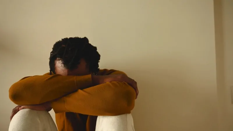 The image shows a person sitting with their head down, visibly distressed