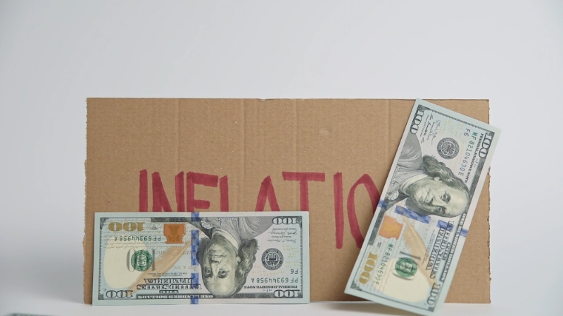 Two $100 bills placed on a cardboard sign with the word 'INFLATION' written in red
