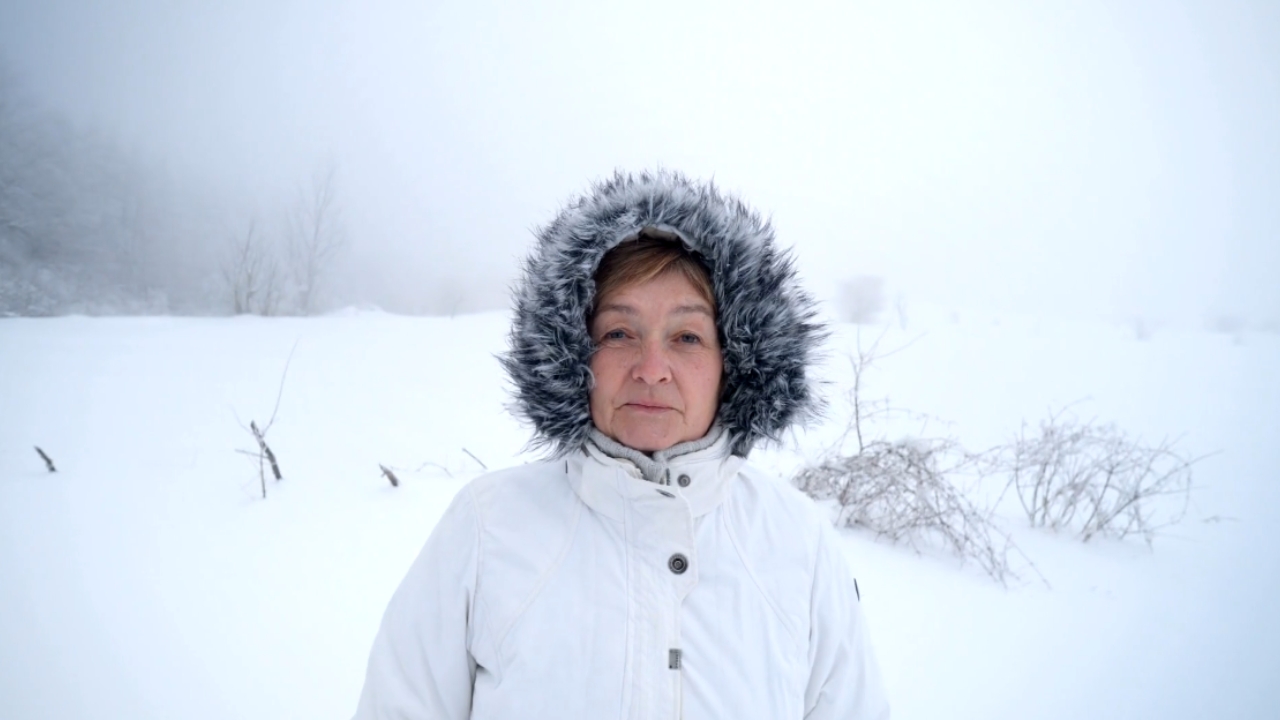 A woman in a white winter coat stands in a snowy landscape