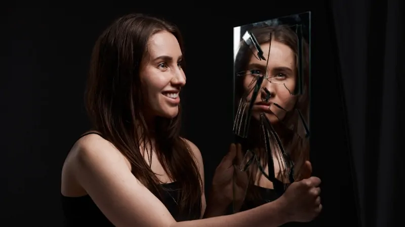 A woman with bipolar disorder holds a broken mirror showing a distorted reflection