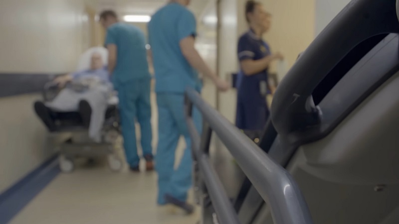 Blurred view of hospital staff in scrubs assisting a patient in a hallway with a hospital bed in the foreground