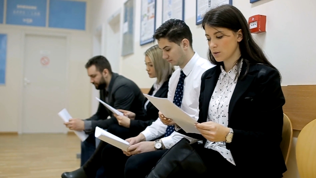 Job seekers sit in a waiting area with application papers in hand