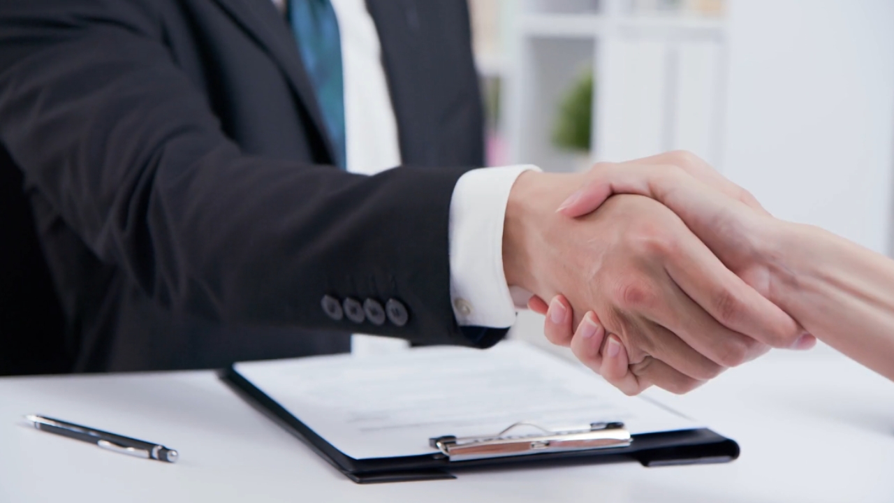 A recruiter and candidate shake hands over a job contract