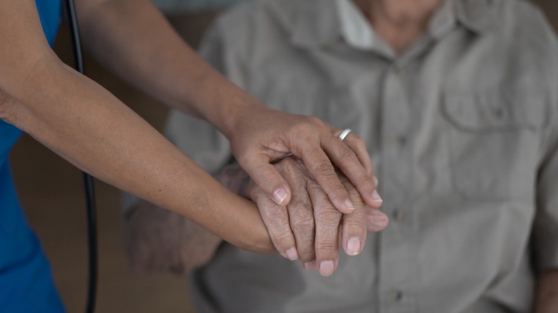 A caregiver gently holds an elderly person's hand, showing a moment of support in a home healthcare setting