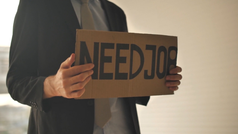 Person holding a cardboard sign that says "NEED JOB"