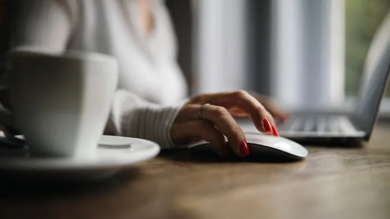 Person using a computer mouse while sitting at a desk with a cup of coffee